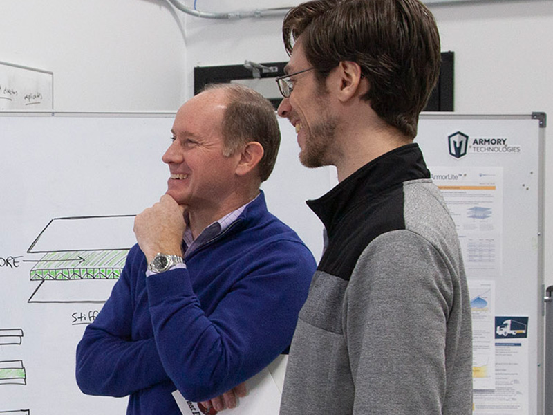 paul dowd and jesse silverberg smile as they consult a whiteboard in the Armory workshop
